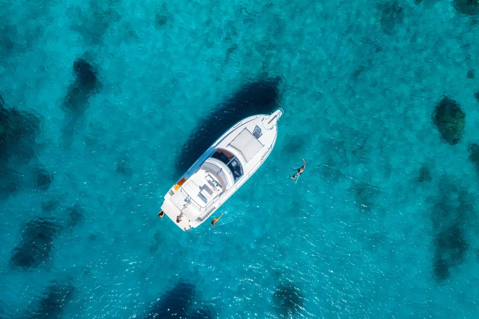 Aerial view capturing a white yacht gracefully floating on crystal-clear turquoise waters, with tourists happily swimming nearby and savoring a sunny summer day in a tropical paradise